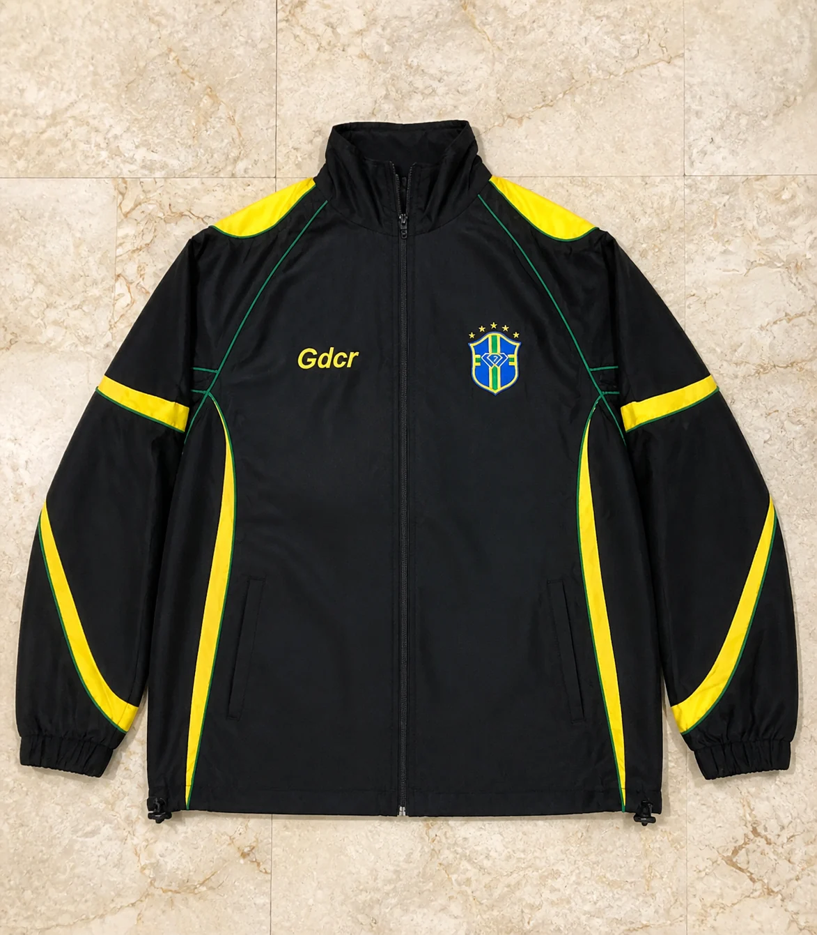 Black track jacket with yellow and green cut-and-sew panels, piping, and embroidered chest details